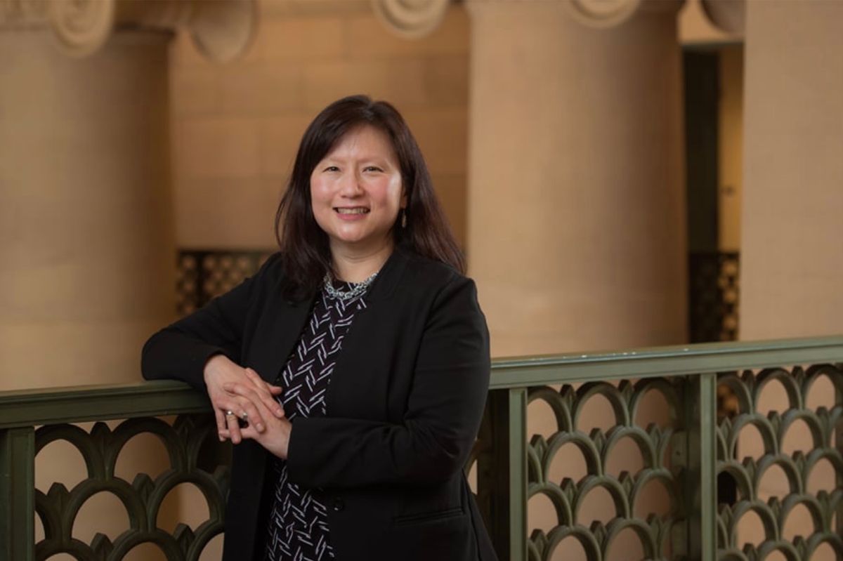 Dark haired smiling woman standing with her arm propped on an ornate green metal railing.